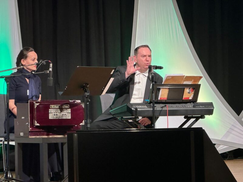 Kongress der Potentialentfaltung in Gmunden. Emanuel und Elisabeth sitzen auf der Bühne und singen und spielen Keyboard und Harmonium